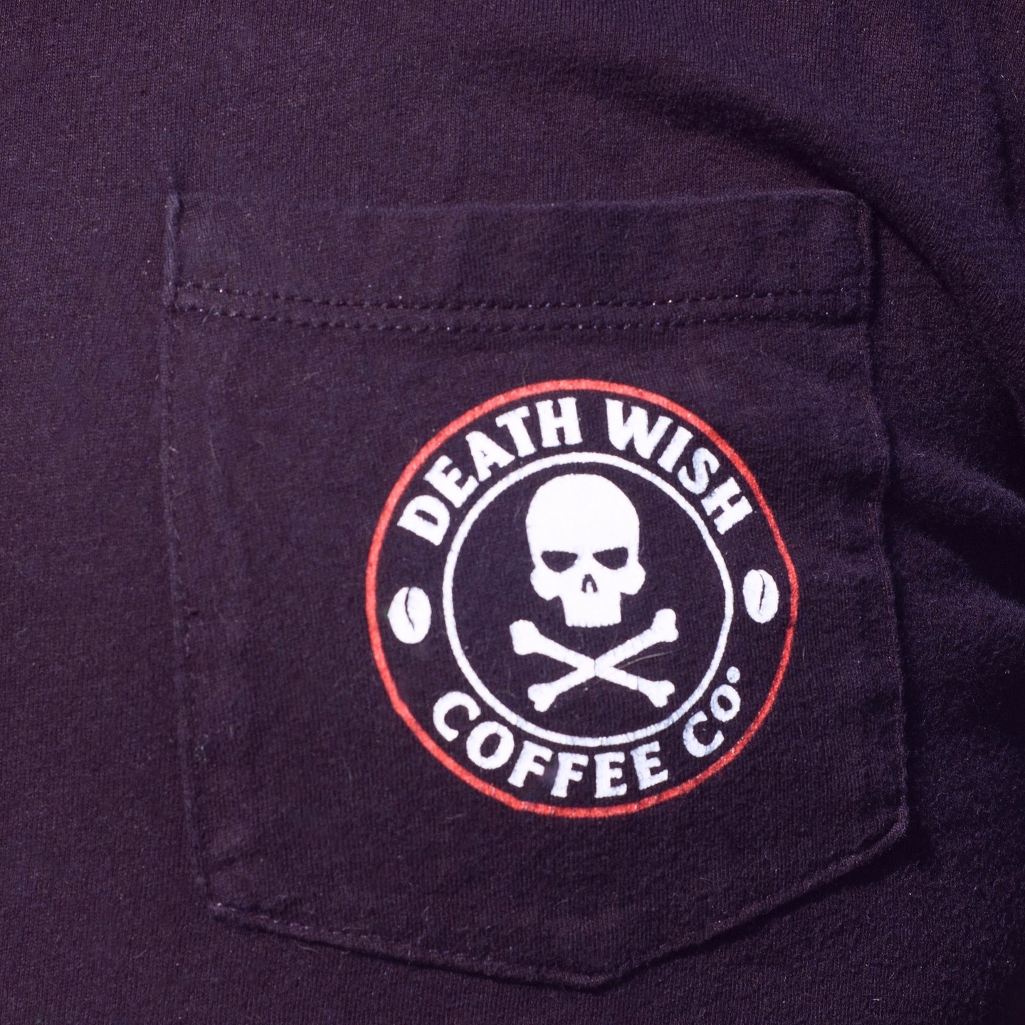 Close up of a logo for 'Death Wish Coffee' on the breast pocket of a black t shirt.