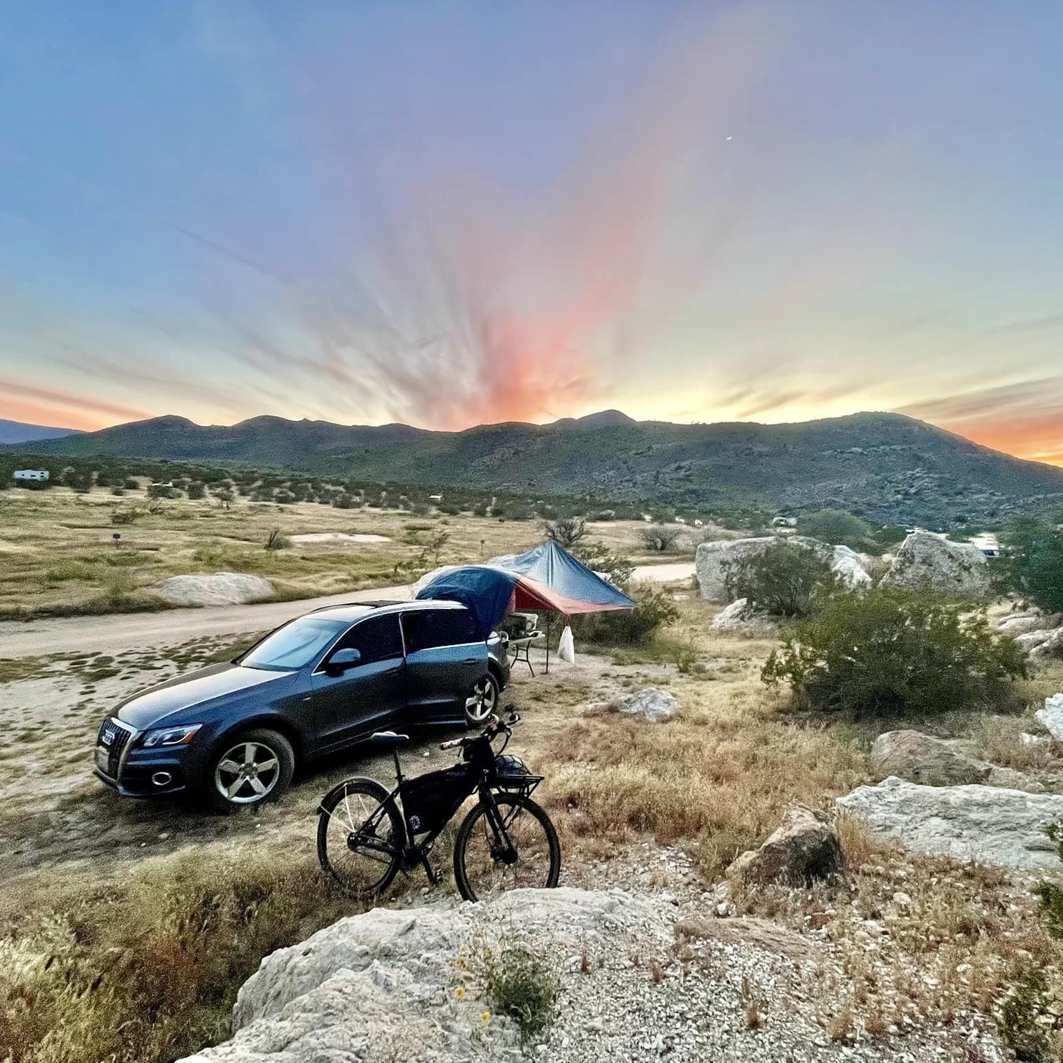 Car parked in the desert with mountains behind it and sunset colors above